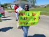 A worker holds a sign that says "Wake up. Rise up. Step up."